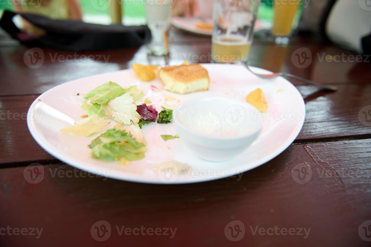 Leftover food on a white plate on wooden table, close-up. Food and drink consumerism. photo