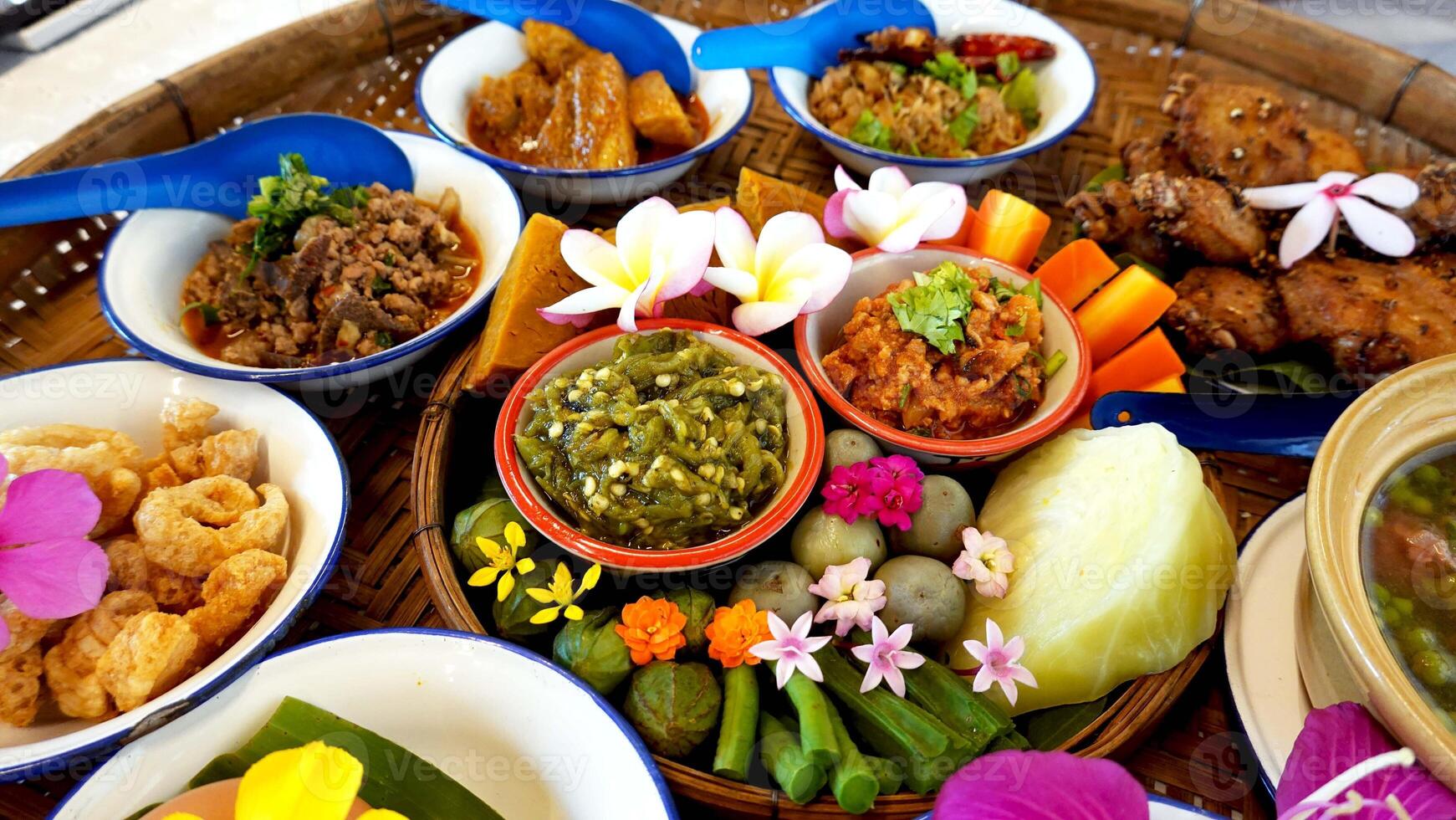 Northern Thai cuisine food set. Pork curry, chilli dip, minced pork salad, soft boiled vegetables and pork snack served in brass dishes. Decorated with flower, garland, spoon and basket background photo