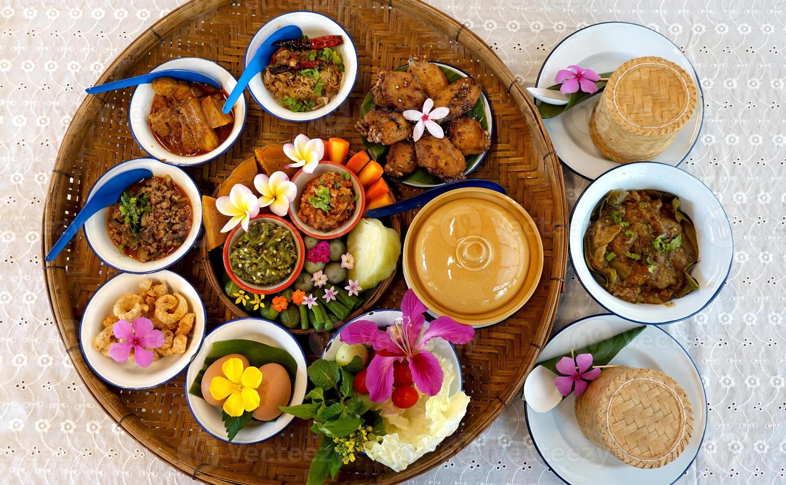 Northern Thai cuisine food set. Pork curry, chilli dip, minced pork salad, soft boiled vegetables and pork snack served in brass dishes. Decorated with flower, garland, spoon and basket background photo