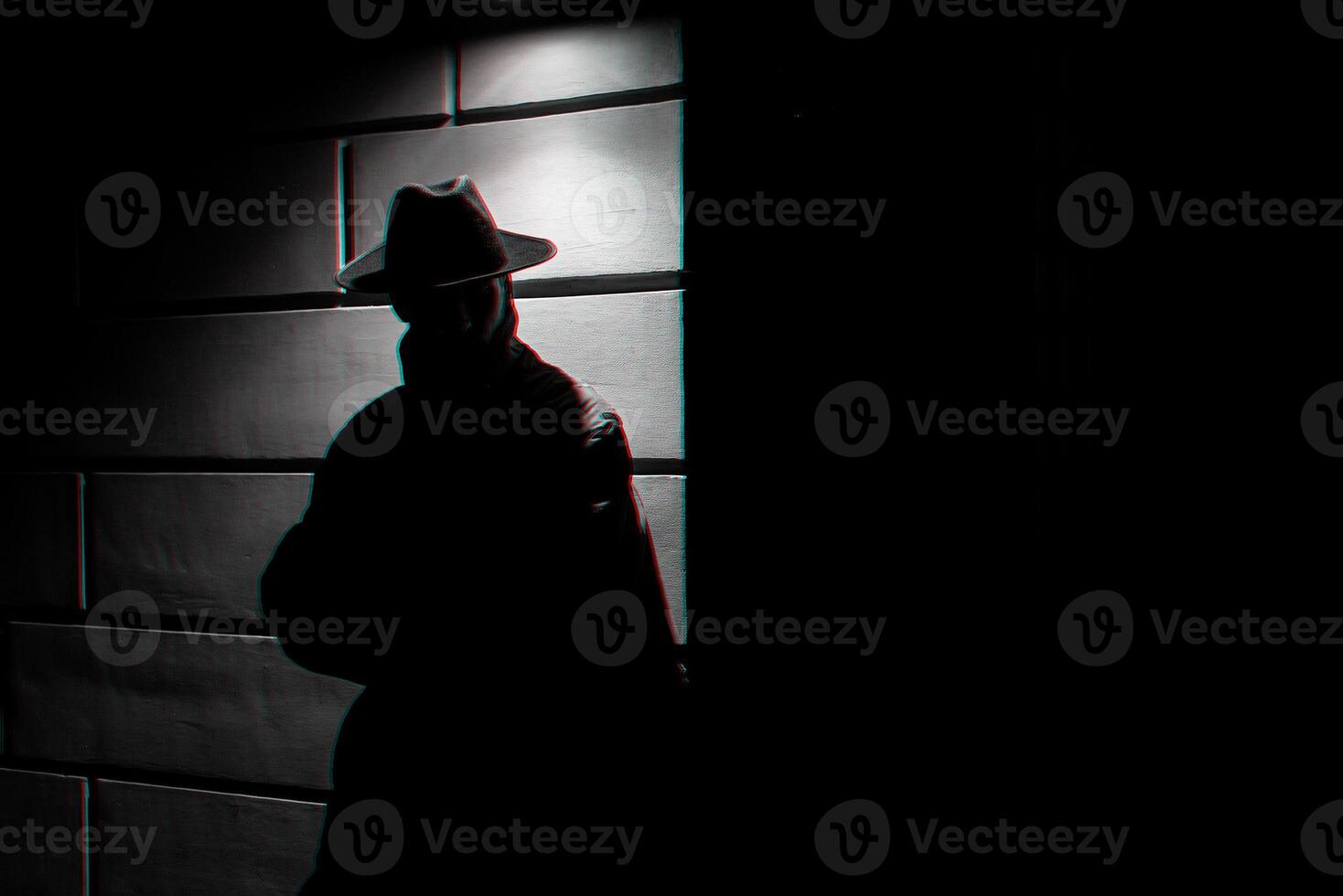 dark silhouette of a man in a raincoat with a hat at night photo