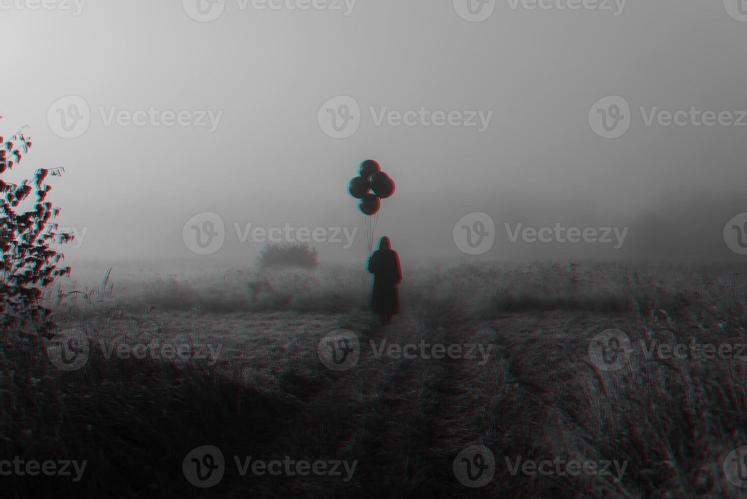 terrible man in a hooded cloak with balloons in his hand stands in a foggy field photo