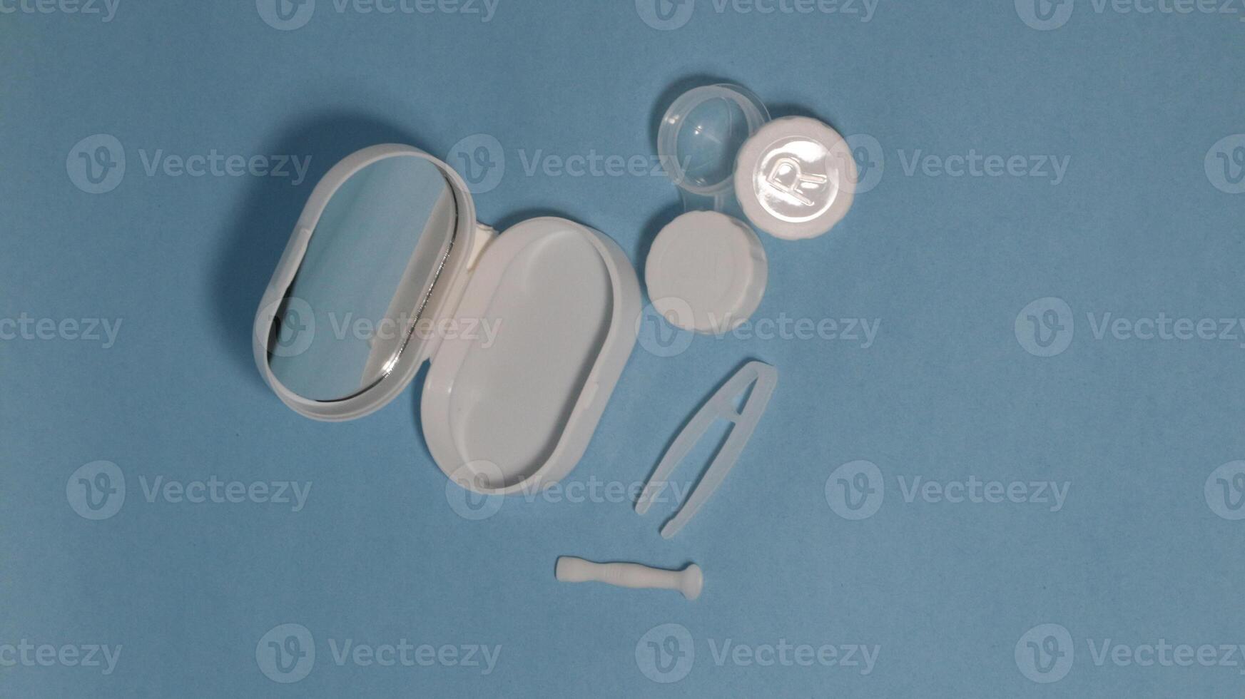 Container with tweezers, holder and contact lenses on a blue background photo