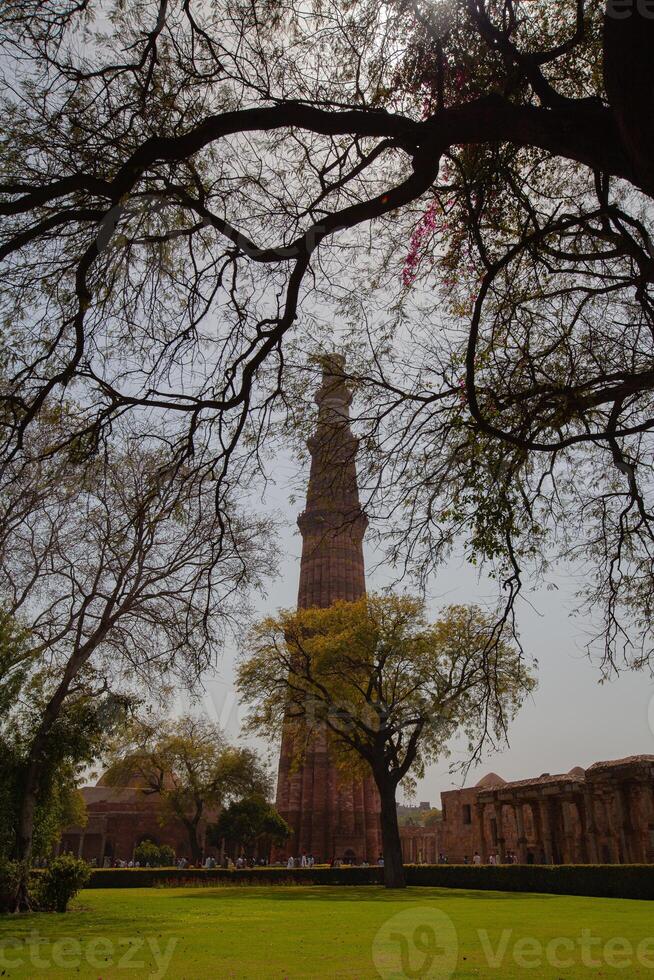The ancient tower is made of red bricks. There are trees in front photo
