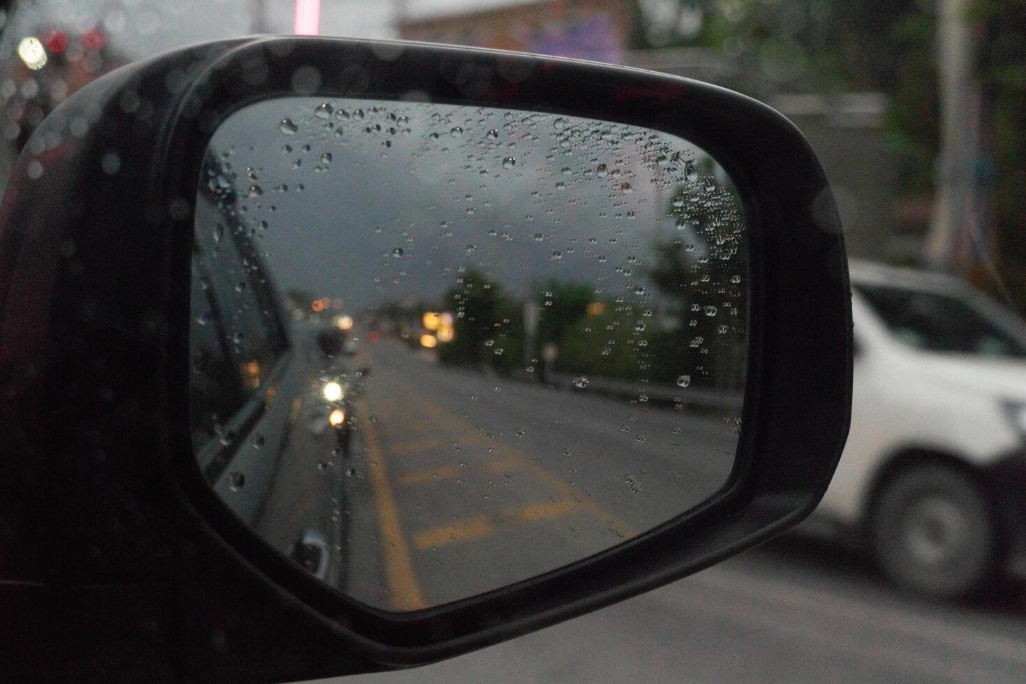 Abstract mirror wing of car with drop of water rain. Looking back for trip yellow line in center of road. Under dark sky in the rainy time. Traffic of many car jam on the road. photo