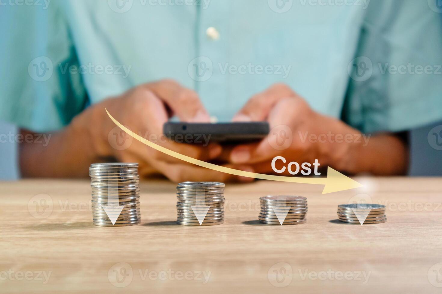Coins stacking with the down arrow and man using a smartphone to recalculate the cost. Cost reduction concept. photo