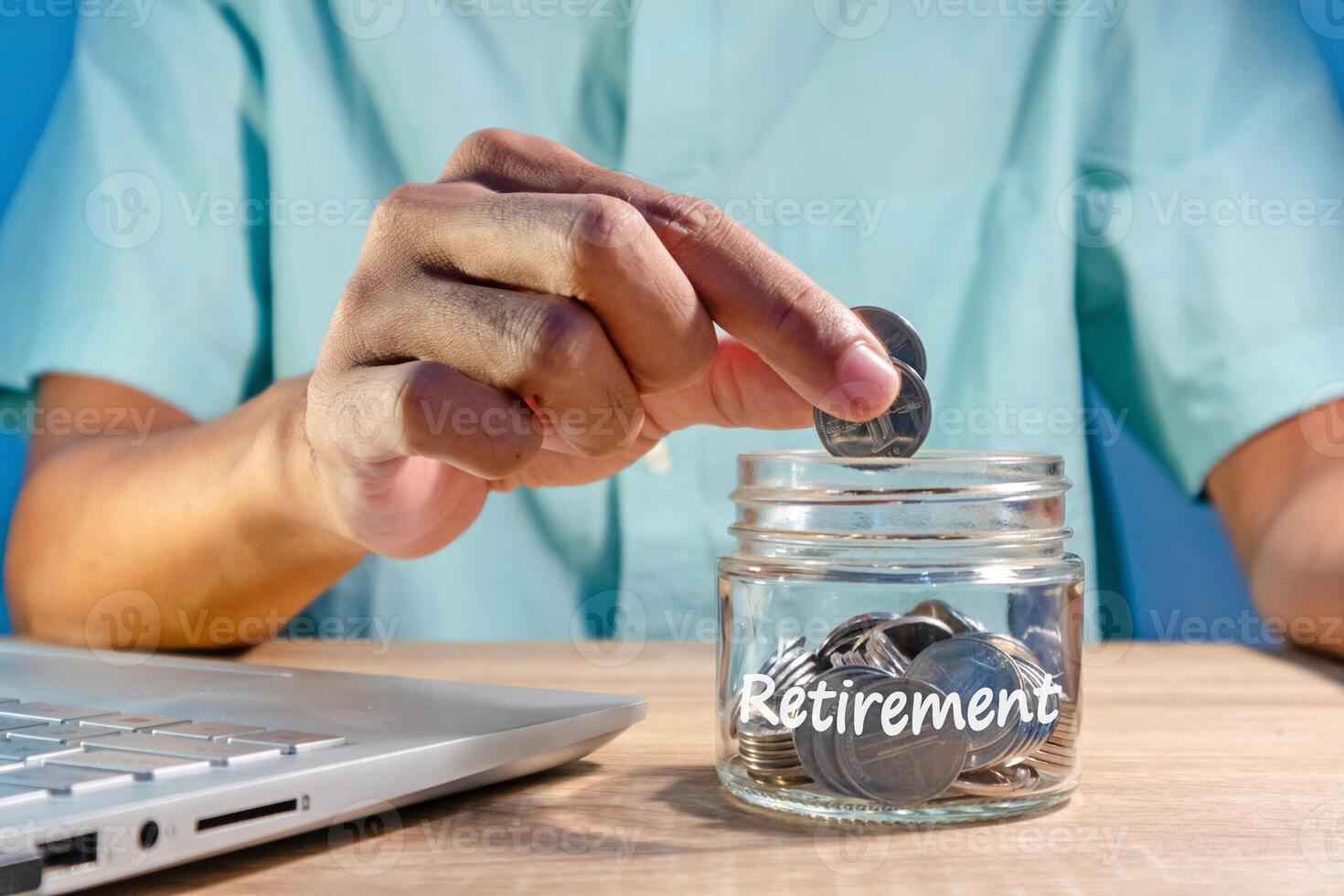 Man working with a laptop and putting coins into a glass jar to prepare for retirement. Saving money for retirement. photo