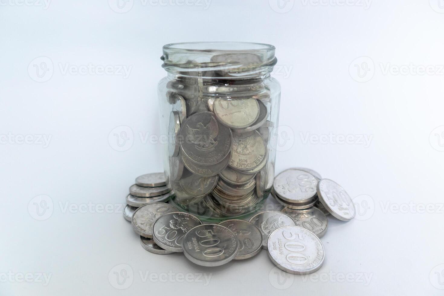 Indonesian Rupiah coins in glass jar and scattered coins with white background photo