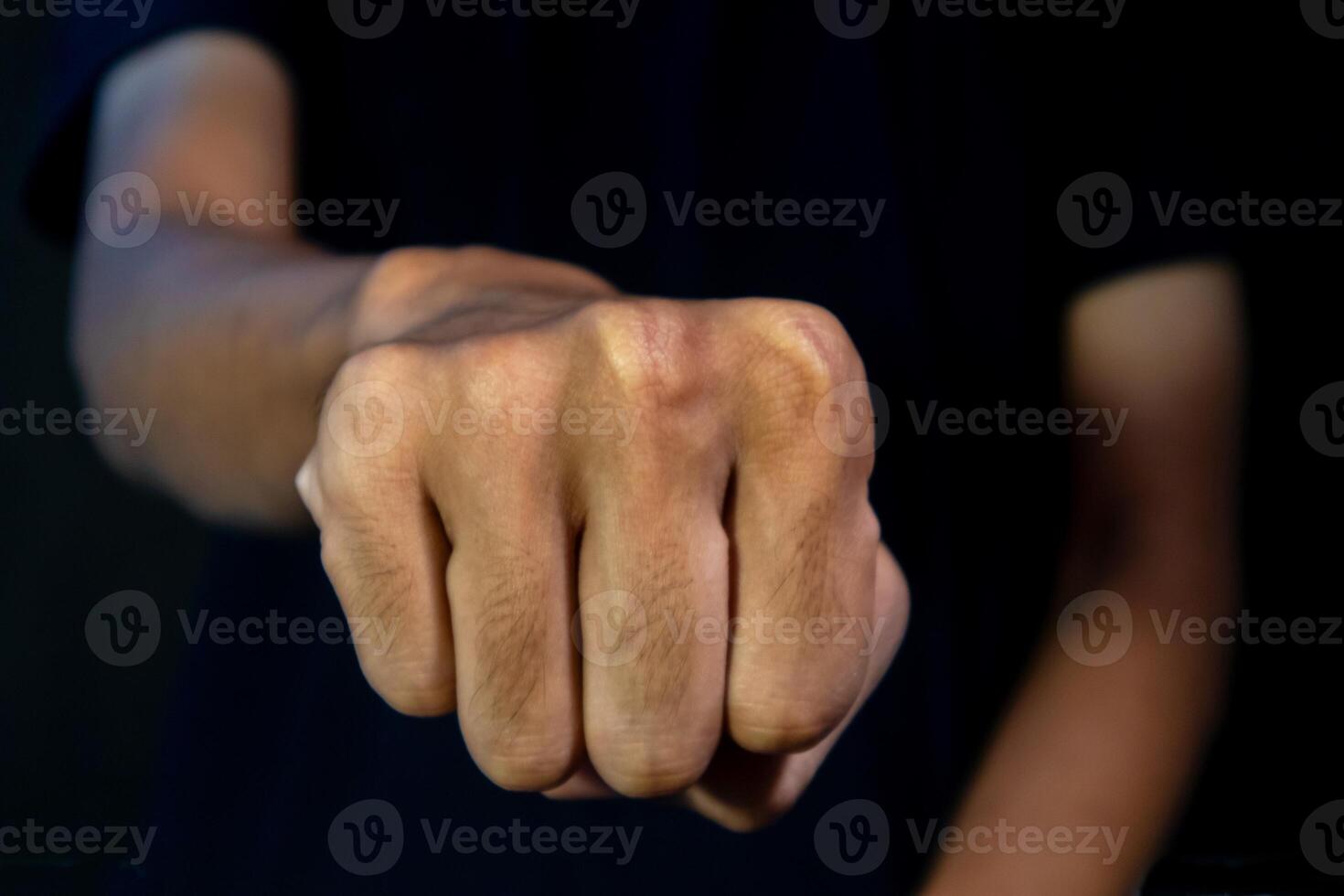 Man with a gesture of clenching his fists forward on dark background. Violence concept. photo