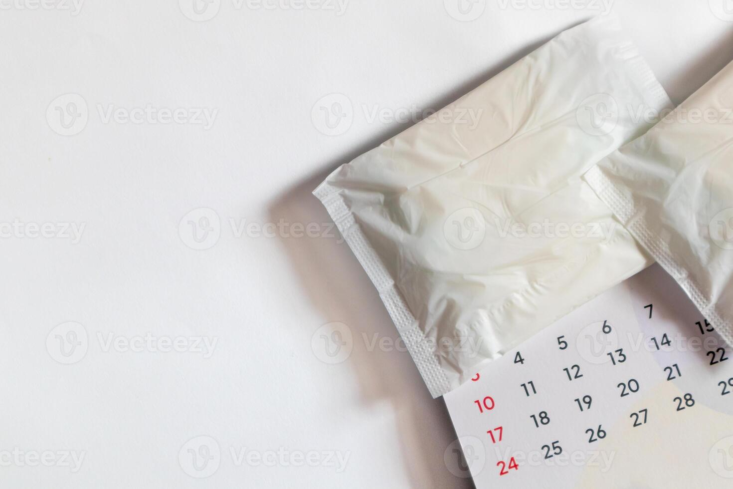 White sanitary napkin and calendar on a white background. Menstrual calendar concept with copy space. photo