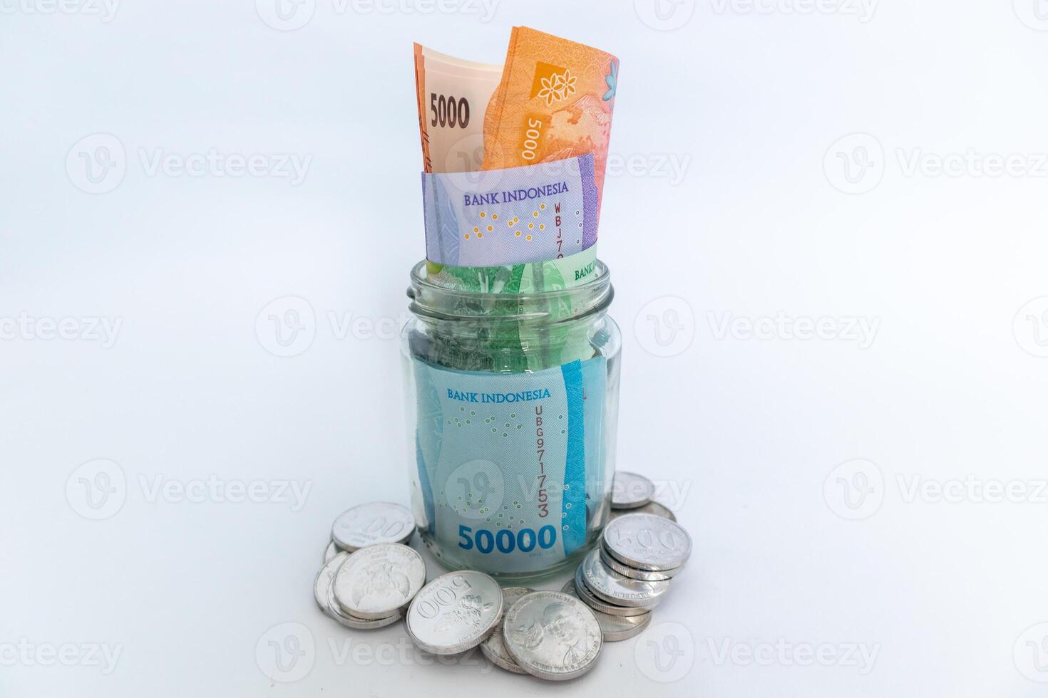 Indonesian Rupiah banknotes in glass jar and scattered coins on white background photo