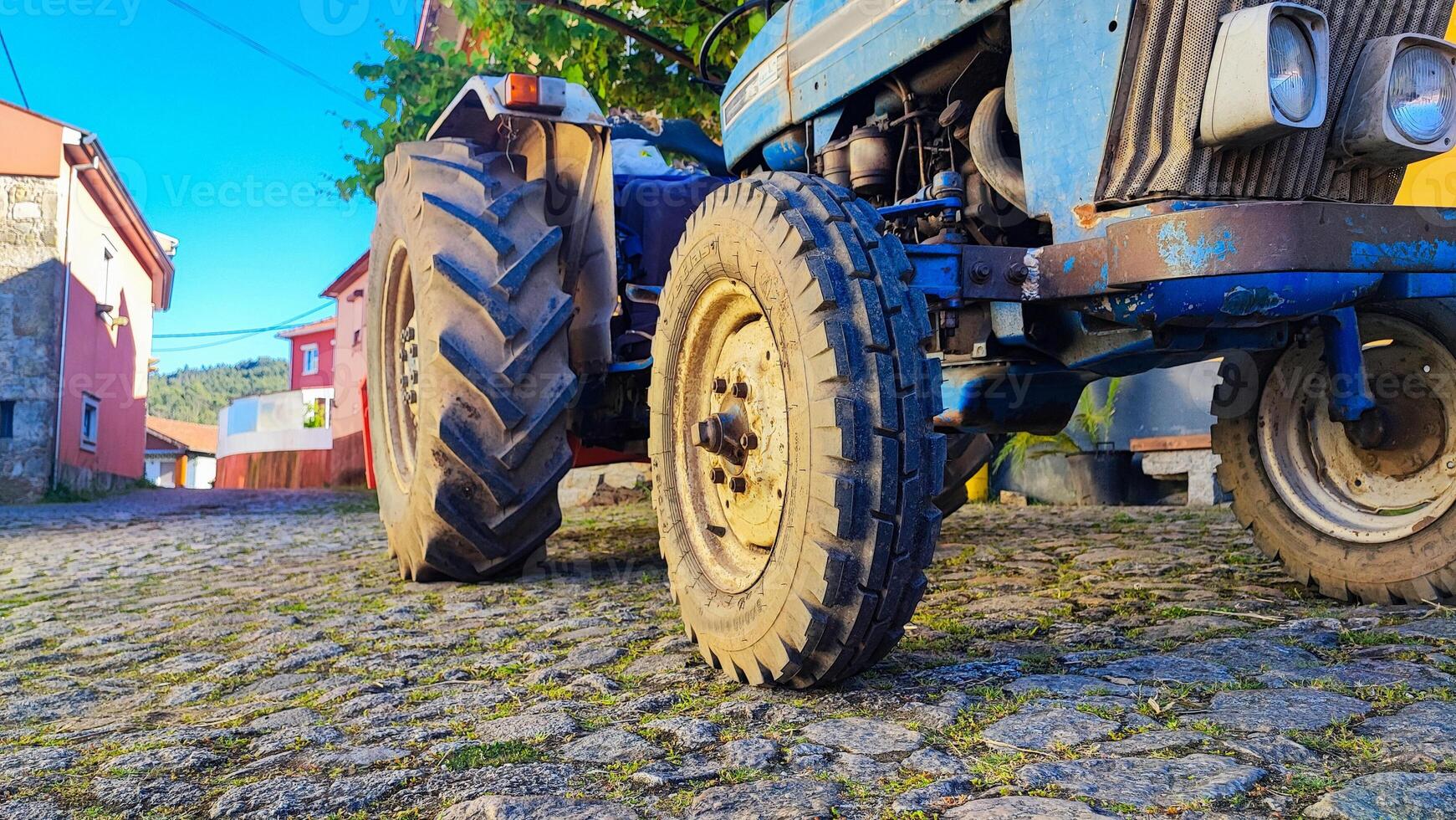 A tractor on an old cobblestone street in a village in Portugal. Close-up of a tractor on a summer village street in Portugal, which stands on the pavement under grapes photo