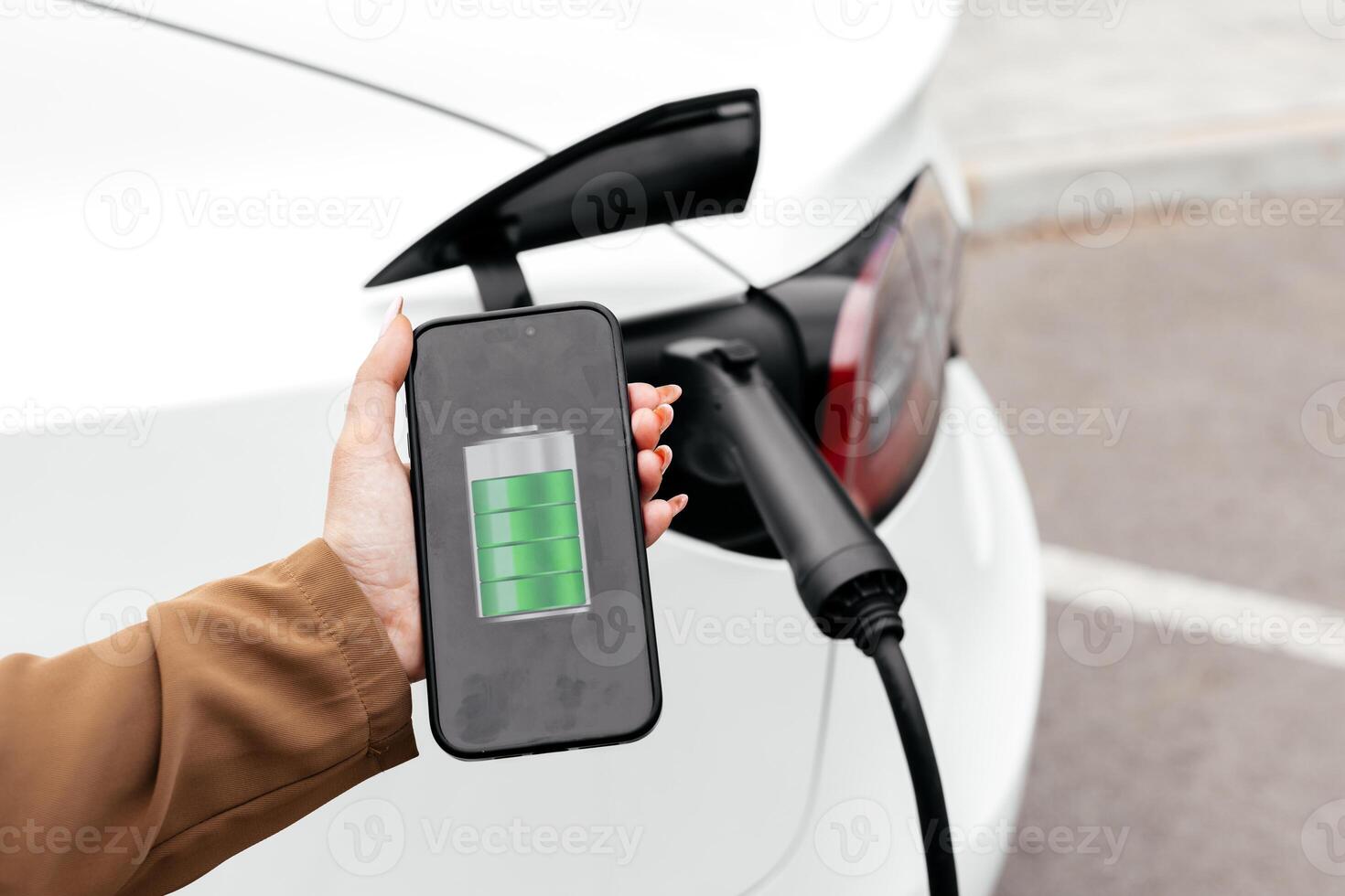 Businesswoman holding smartphone display battery status interface by smart EV mobile application while eco-friendly EV car recharging electricity from charging station photo
