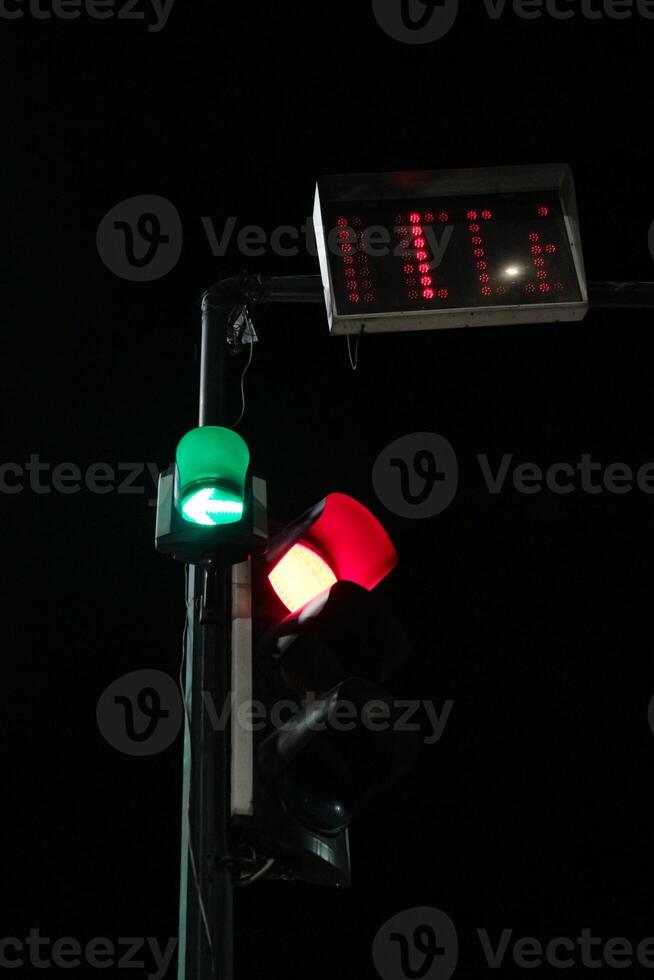 traffic light with a green arrow pointing left, a red light, and a digital countdown timer displaying 11. The scene is dark and quiet, with a sense of anticipation. photo