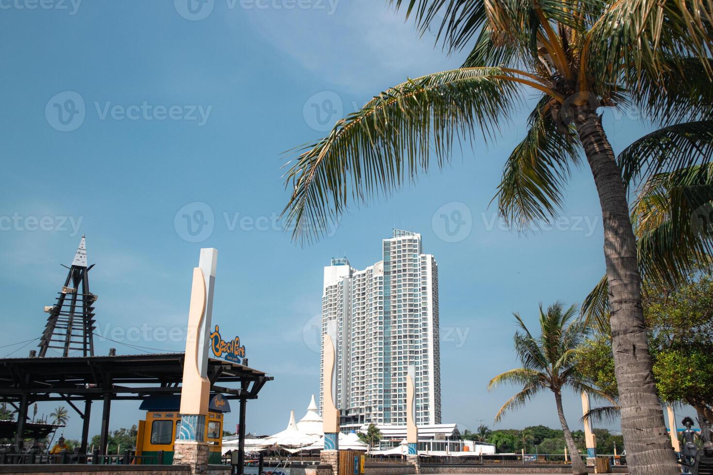 Urban beach park scene with a tall modern building, palm trees, and a clear blue sky, showcasing a blend of nature and architecture in a vibrant city setting photo