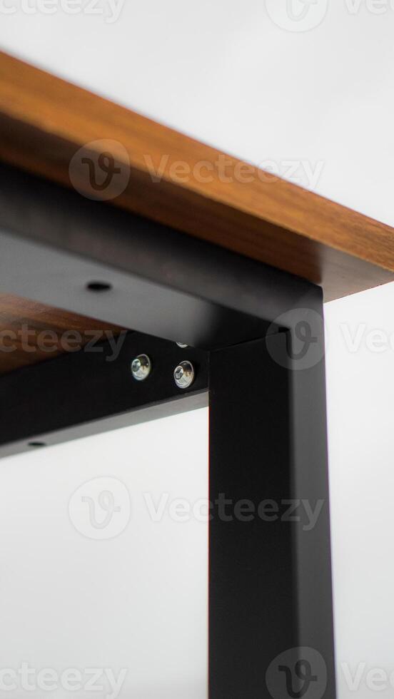 Close-up detail of a wooden table with black metal legs. The image is focused on the junction of the table top and legs, showcasing the sturdy construction and visible screws. photo