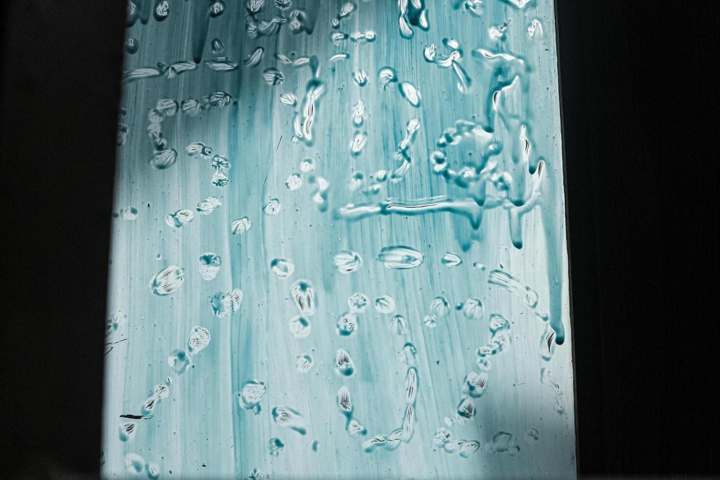 A close-up of a textured glass surface with streaks of blue paint and water droplets, creating a unique and abstract pattern. The light shines through the glass, casting a soft glow. photo