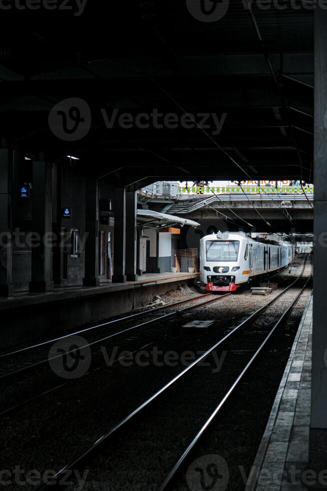shows a commuter line train passing through the platform hallway of BNI city station, which is quite dark during the day. The train is white with red accents, and the platform is empty photo