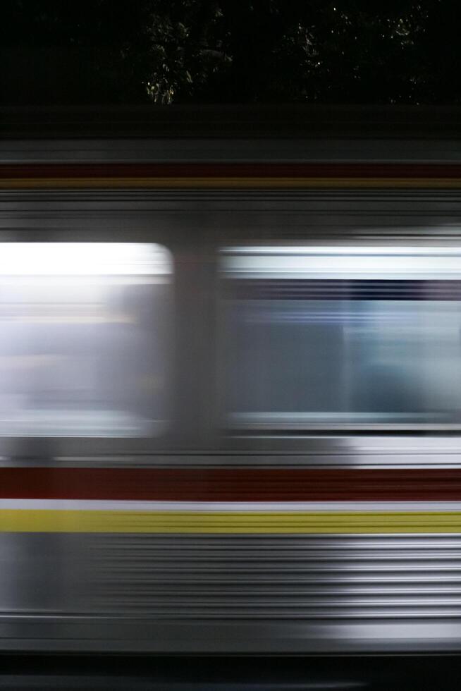 A blurry image of a speeding commuter line train at night, captured with long exposure. The lines of light create a dynamic and abstract composition, highlighting the speed and movement of the train. photo