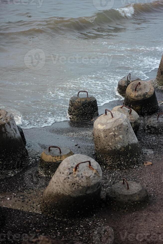 The image focuses on a cluster of concrete breakwaters, partially submerged in the water. The waves are crashing against the breakwaters, highlighting the rugged texture of the concrete. photo