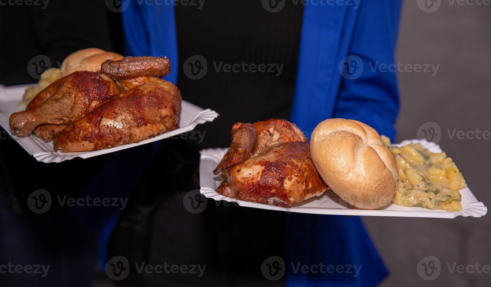 Grilled chicken served on paper plates with bread rolls and potato salad photo