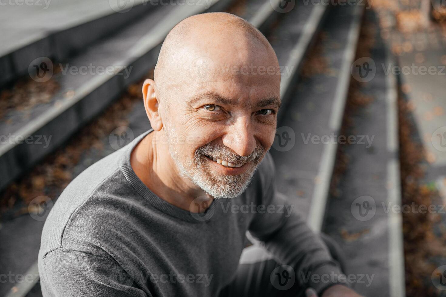 Elderly man sitting on steps, smiling up at camera, autumn leaves scattered around photo