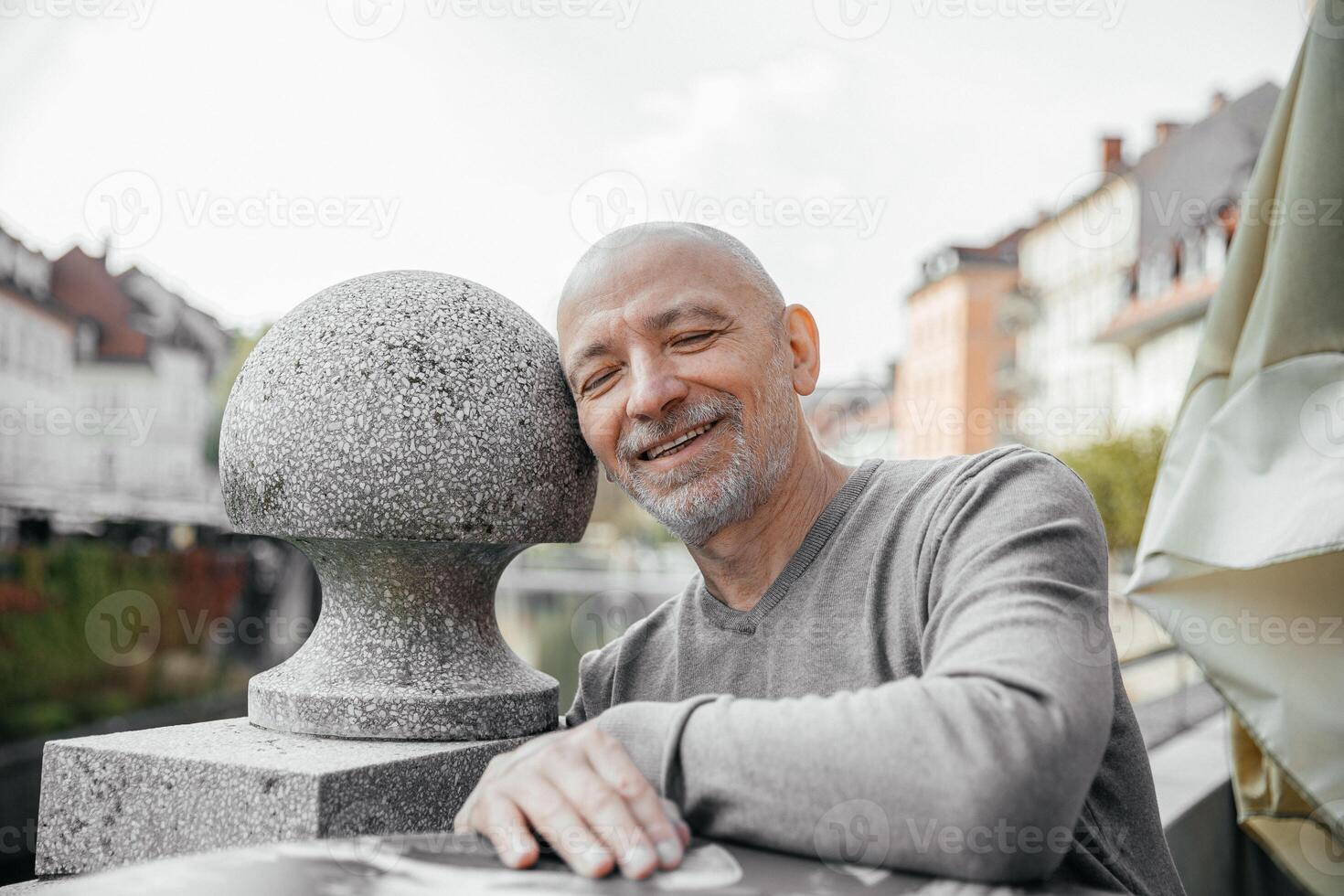 Elderly man with a content smile leaning on a stone sphere in a scenic urban park photo