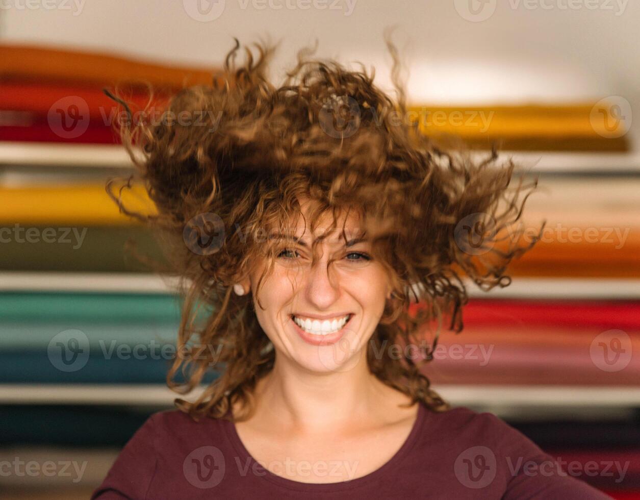A joyful young woman with lively curly hair playfully poses in her colorful fabric shop, radiating happiness and vitality photo