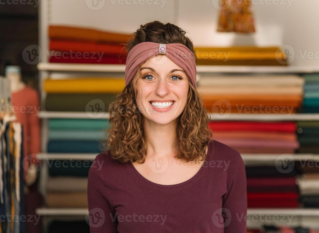 Smiling Fashion Designer in Her Workshop with Colorful Fabric Rolls photo