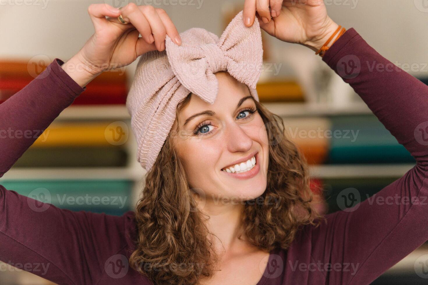 Smiling Designer Trying on a Pink Knitted Bow Headband in Fabric Shop photo