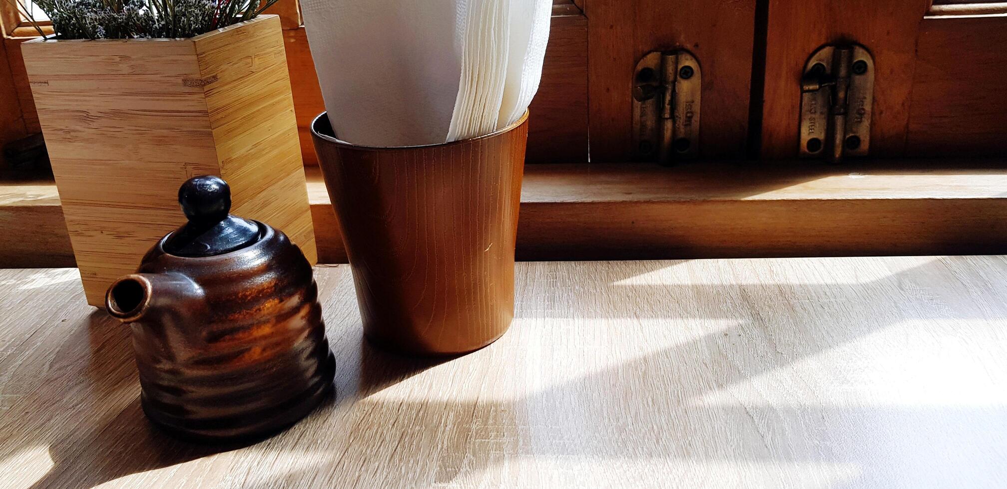Black ceramic tea jug and white napkin putting on wooden table sunlight and copy space. Object, Design and Natural material concept. photo