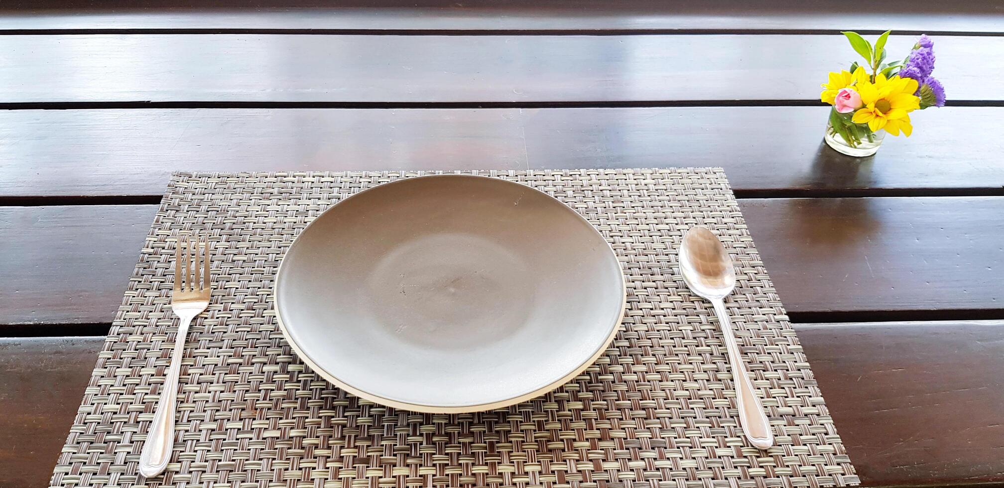 Gray Plate with spoon and fork putting on wooden table for customers to eating food with beautiful flower in glass decorated and copy space at restaurant. Preparation, Service and Arranged concept. photo