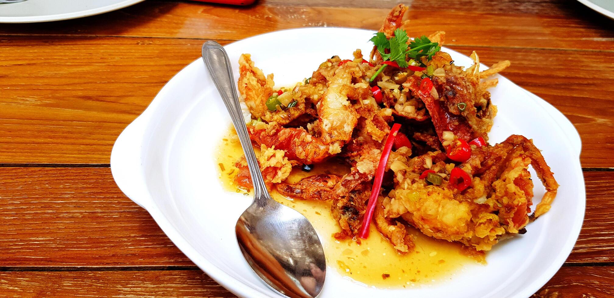 Close up roasted crab with Chili and Salt in white plate with spoon on wooden table with copy space. Spicy food, Delicious, Seafood and Special menu concept. photo