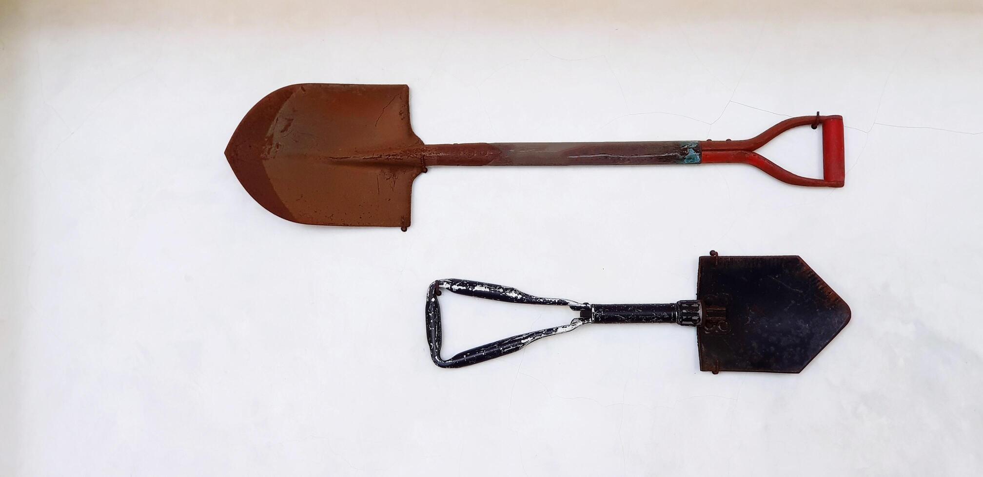 Two rusty hoe, mattock, spade or shovel hanging on the white concrete wall. Object, Decoration, Tool and Equipment for Agriculture and Construction concept. photo