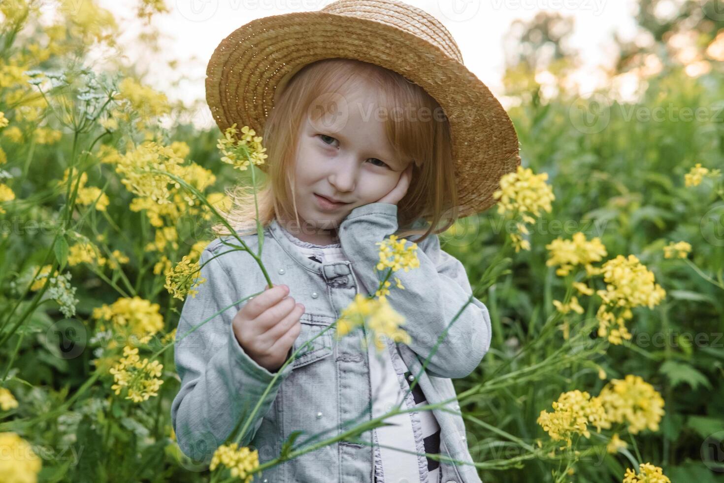 Blonde girl in a field with yellow flowers. A girl in a straw hat is picking flowers in a field. A field with rapeseed. photo