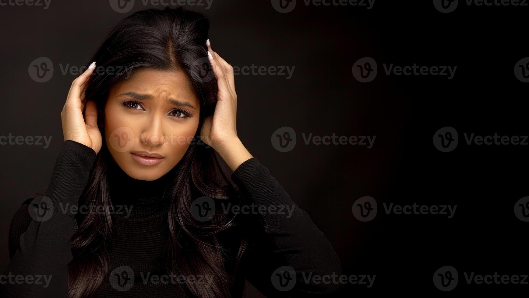 An attractive Indian woman holding her head in pain and looking at the camera isolated on a black background photo