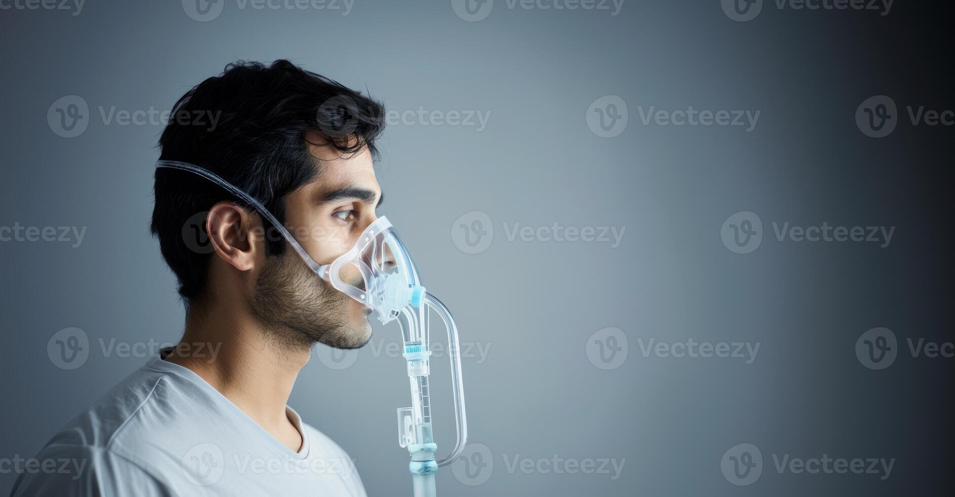 A young Indian man using a nebulizer for relief from breath issues on a grey background photo