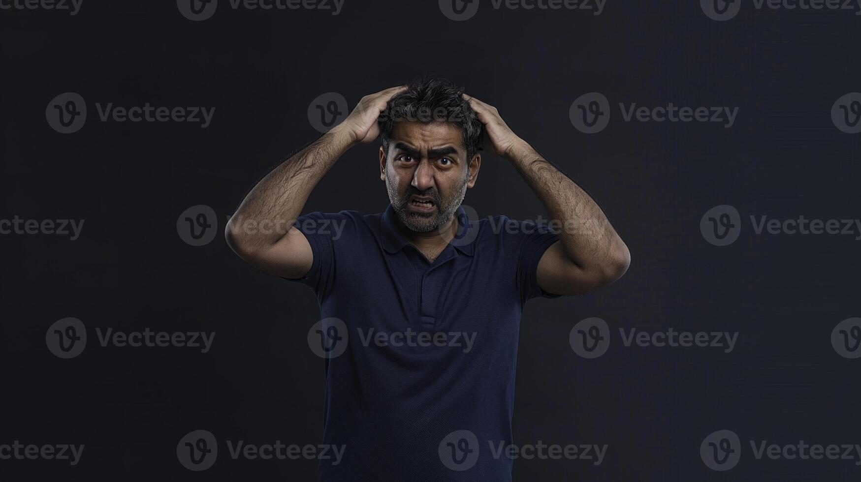 An Indian man hands on head holding hair with a distressed expression looking at the camera photo