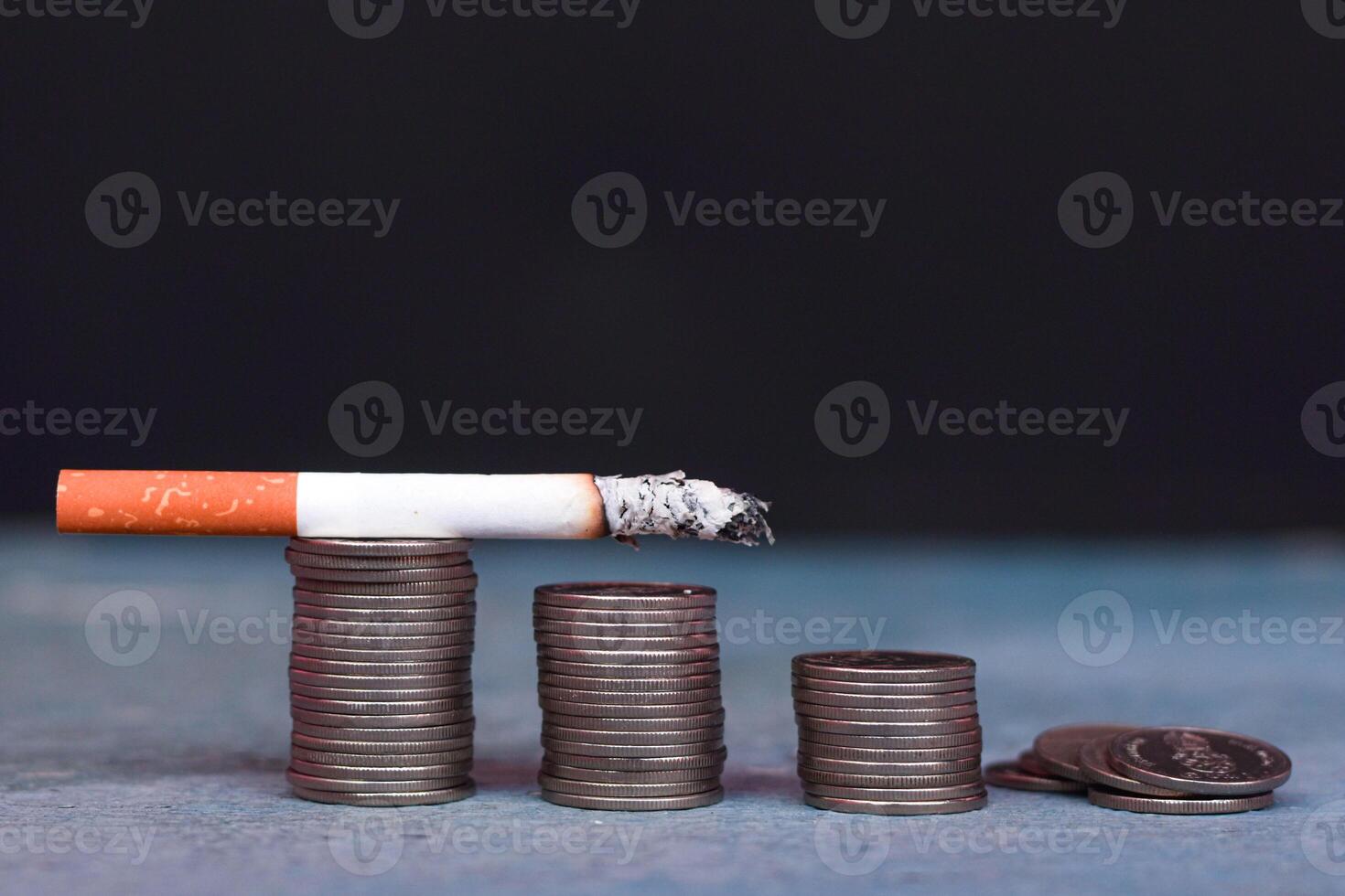 A lit cigarette was slowly being extinguished, placed on top of a pile of coins. Cigarette concept. photo
