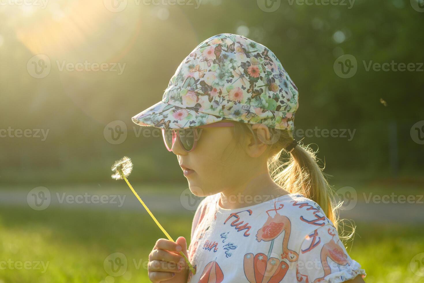 Cute little girl blowing dandelion seeds in spring sunset photo