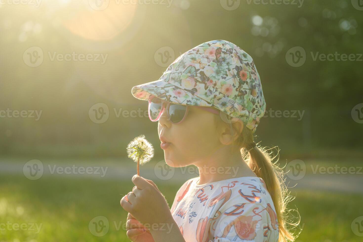 Cute little girl blowing dandelion seeds in spring sunset photo