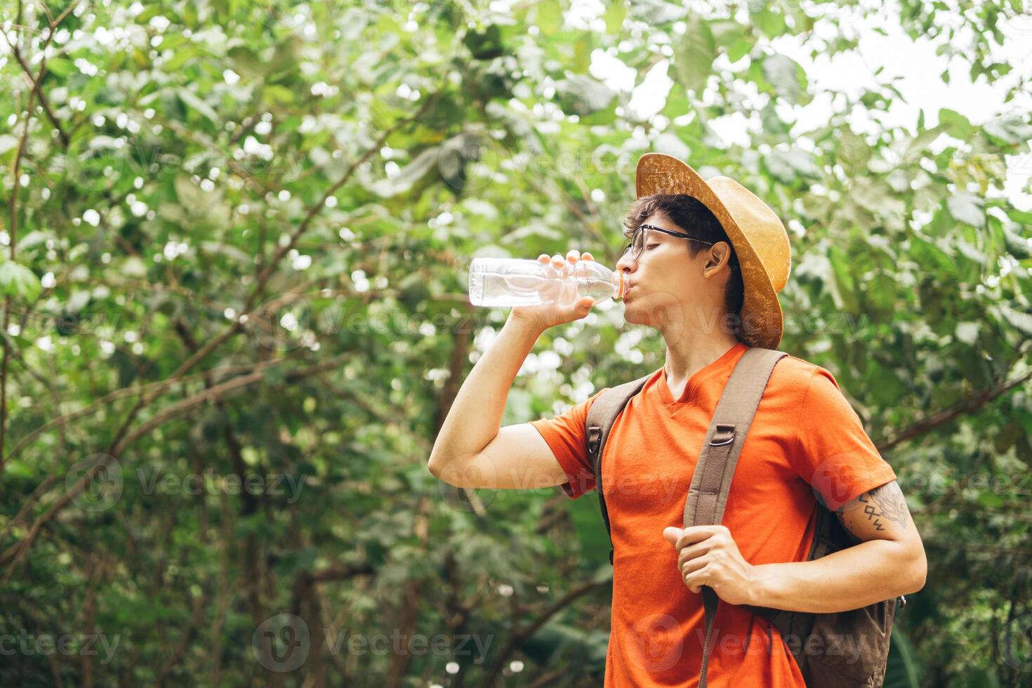 Thirsty man drinking water while hiking by forest. photo