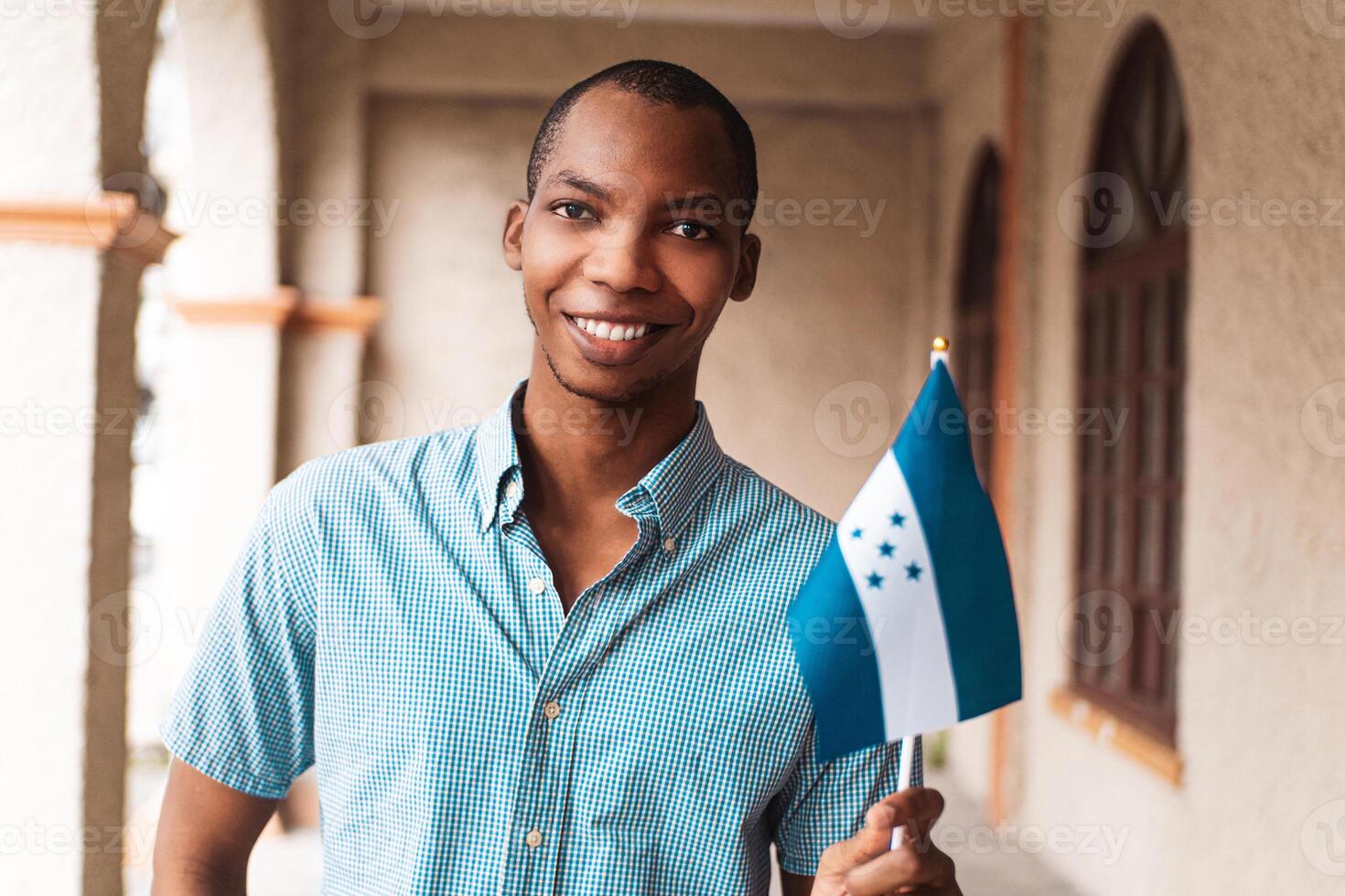 Close up portrait of a young african descent man looking at camera holding a small flag of honduras. photo