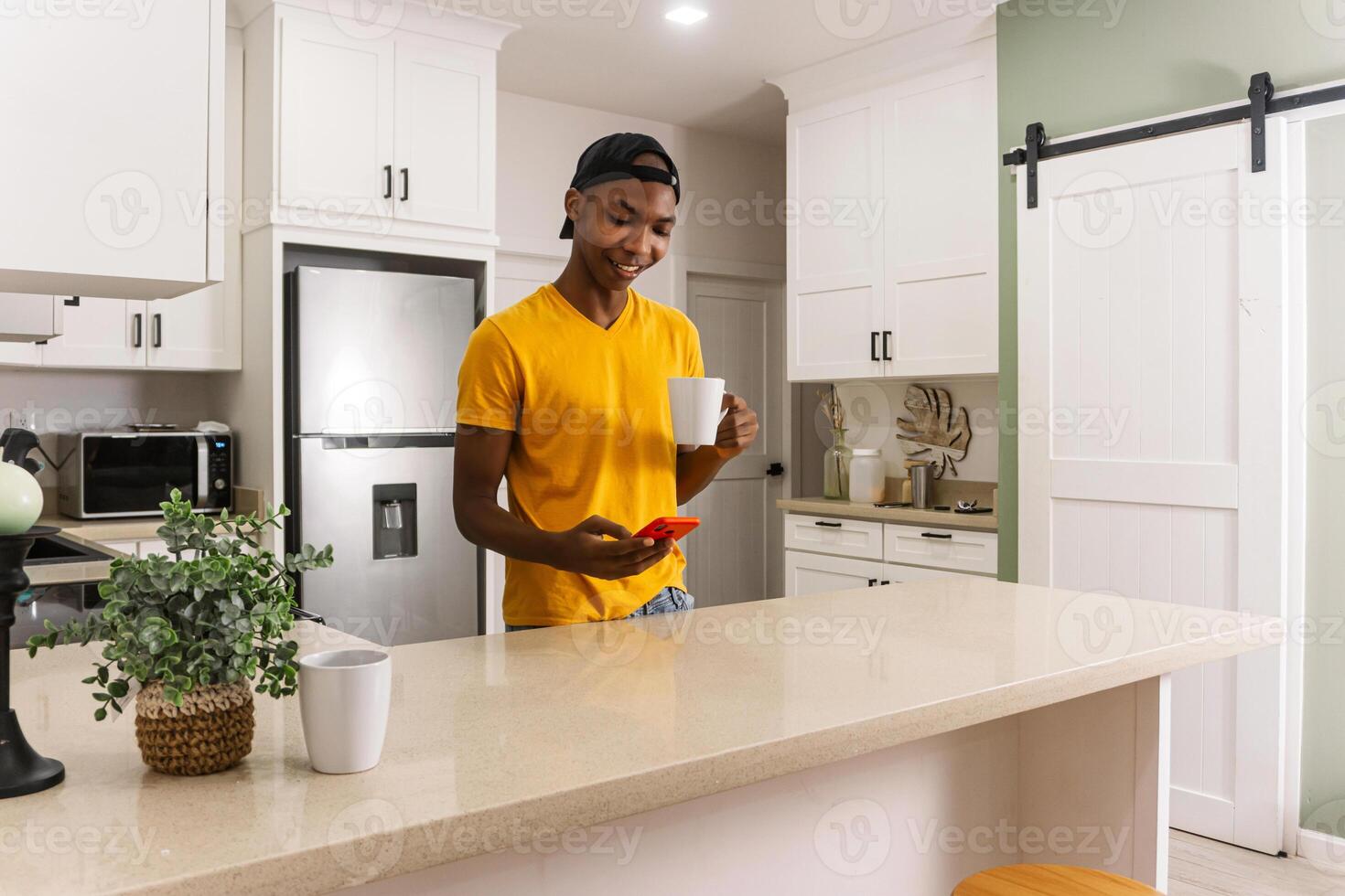 Young african man in the kitchen with a cup of coffee and using a phone. photo
