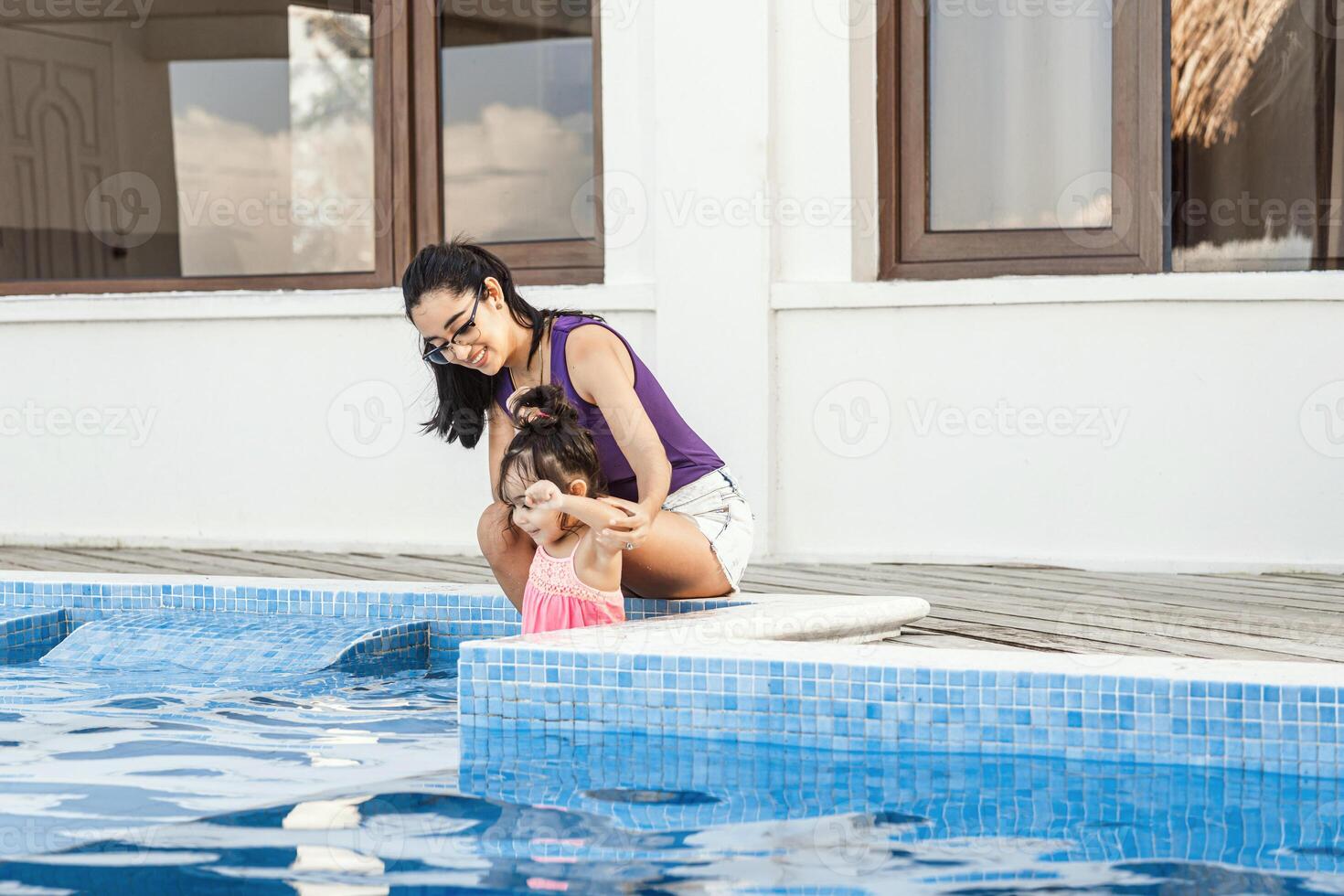 Latin american mother enjoying summer vacation in a pool with her daughter. photo