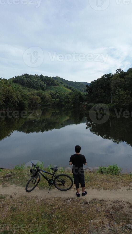 Man Resting with His Bicycle by the Lake, Enjoying the Beautiful Summer Morning Background photo