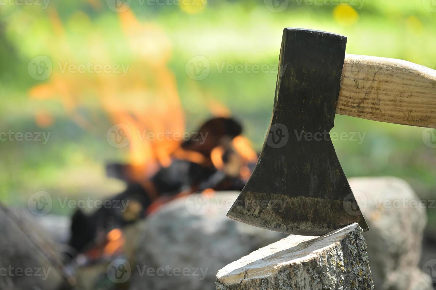 Hatchet embedded in a log of wood opposite campfire photo