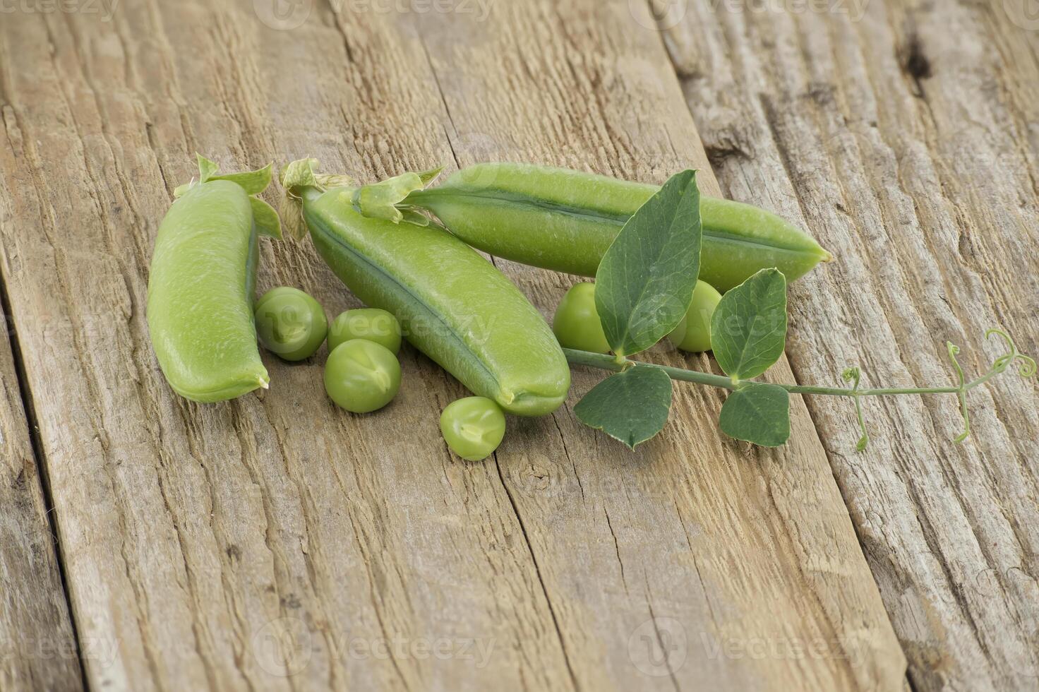 Group of fresh green peas with leaves on wooden surface photo