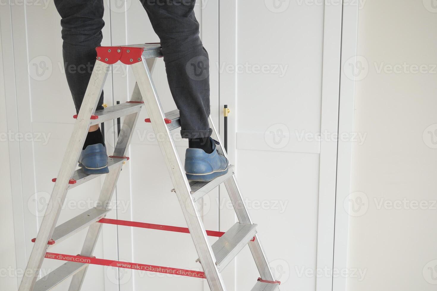 A person is using a ladder indoors to work on white cabinets for a home improvement project photo