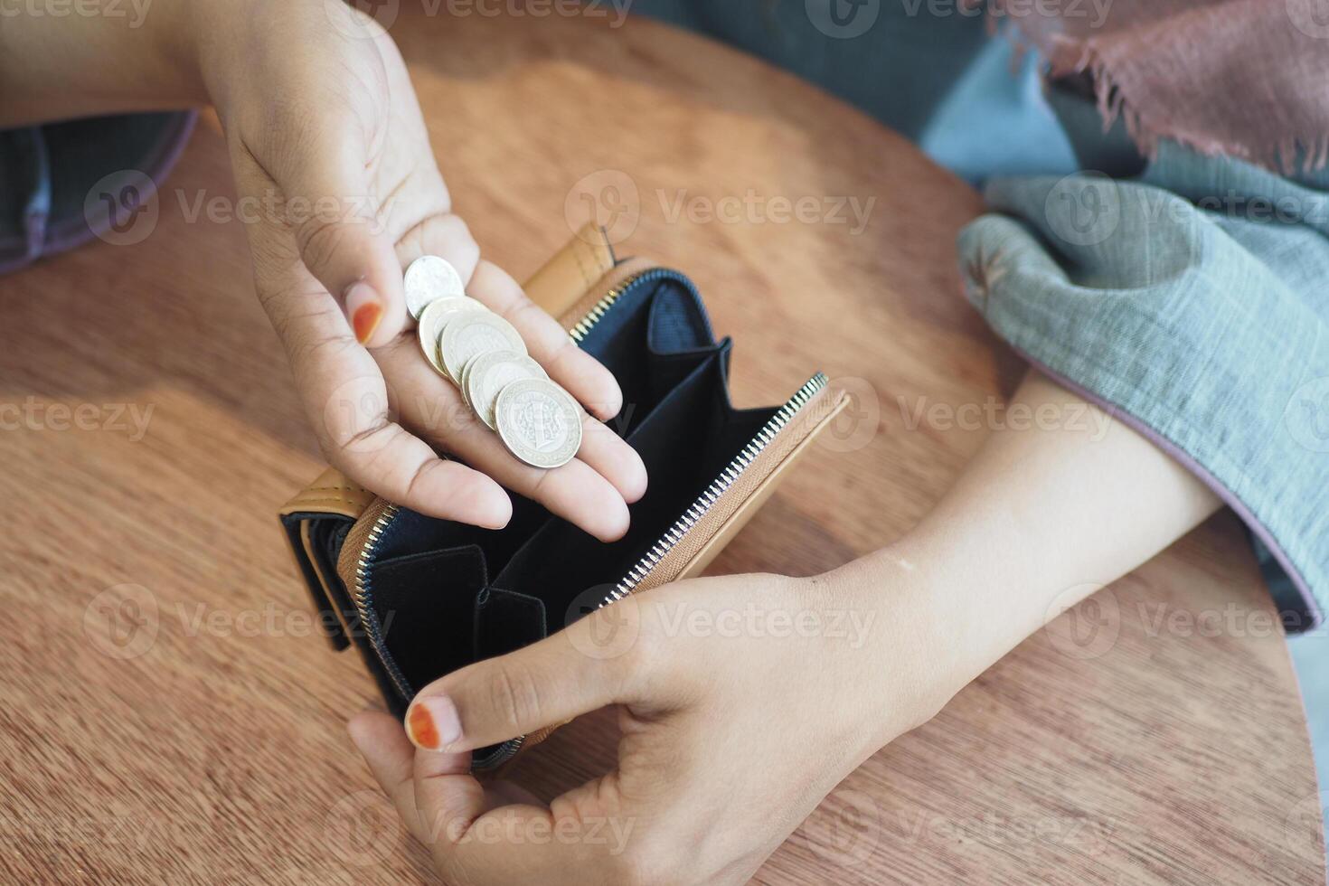 Closeup photo of a female hand holding coins near an open wallet on a wooden table