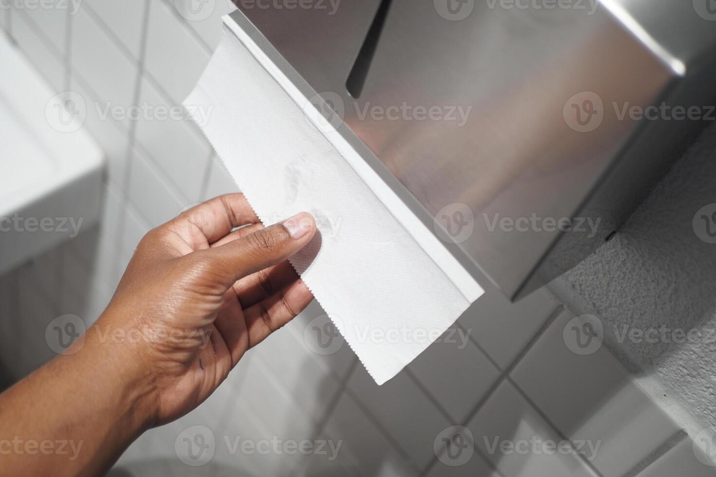 Hand Using Paper Towel Dispenser in a Hygienic Public Restroom with Clean White Tiles photo